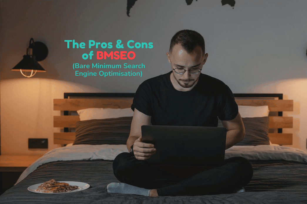 A man works on his laptop while sitting in bed beside a pizza.
