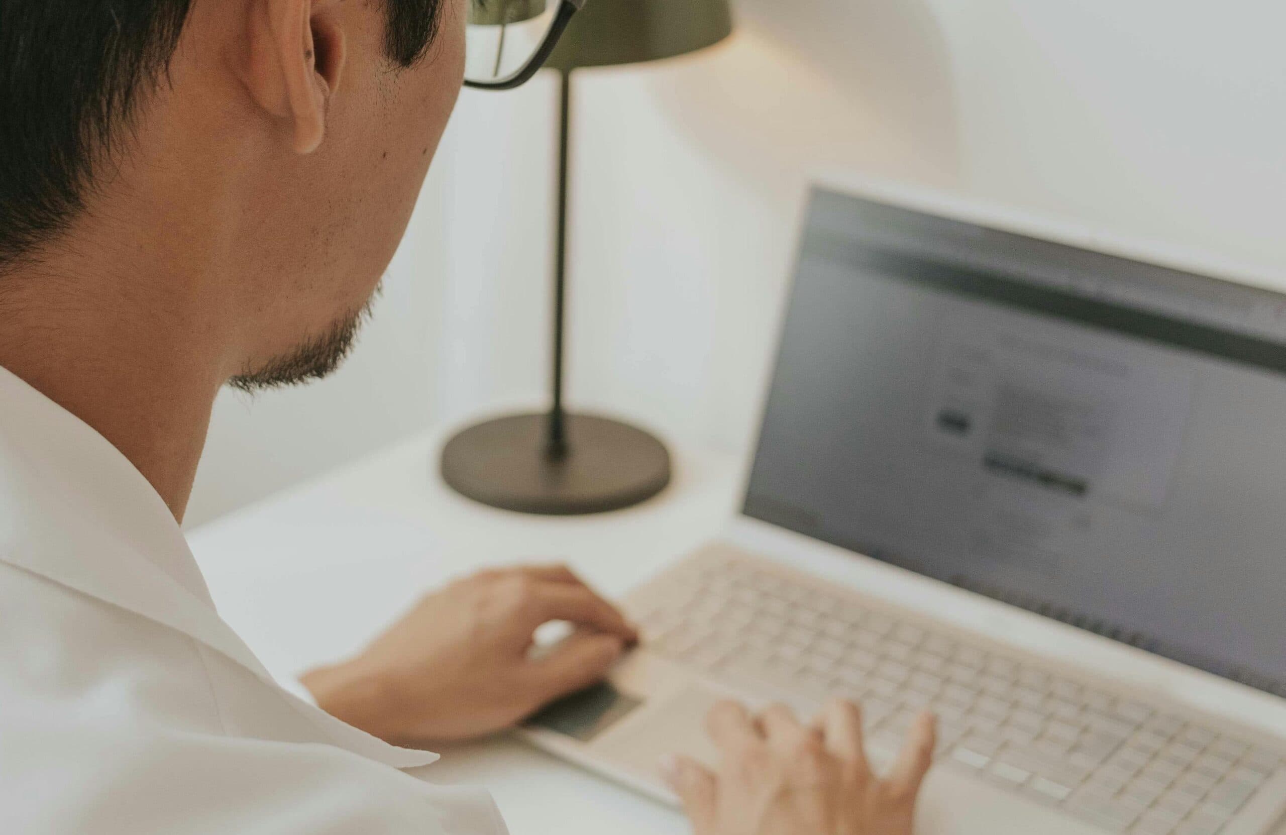 A man types on a laptop in a bright room.