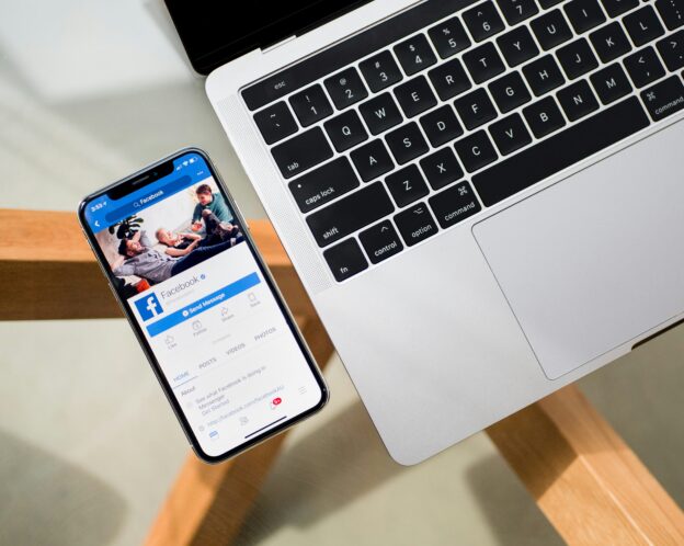 An open Facebook app on a phone next to a computer