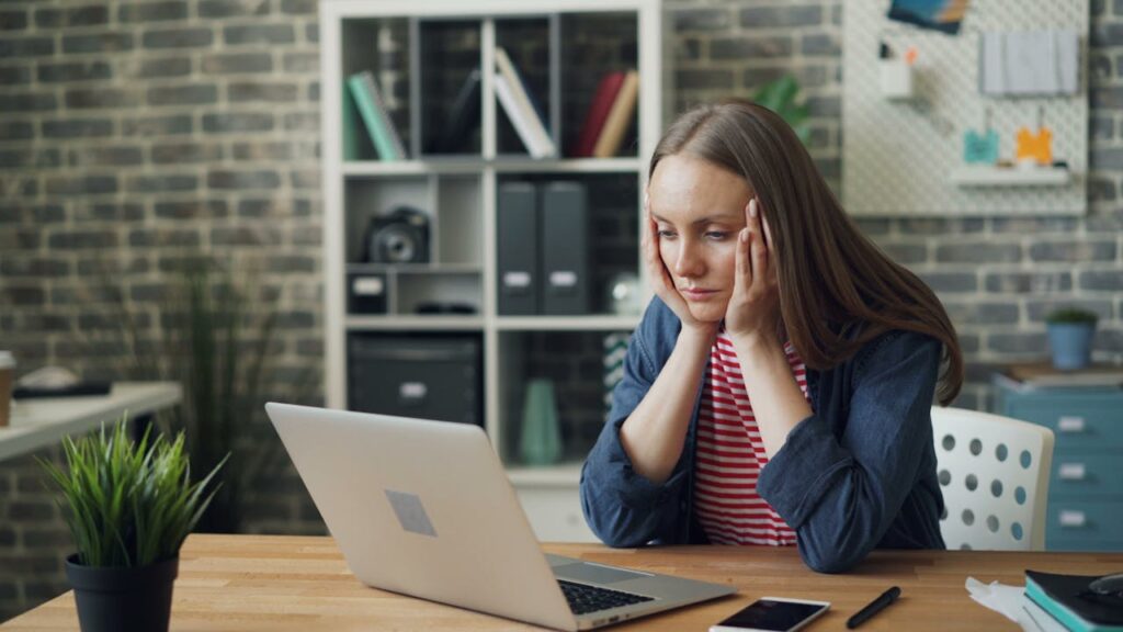 A woman puts her head in her hands while looking at her laptop.