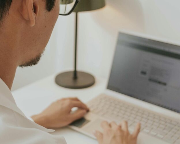 A man types on a laptop in a bright room.